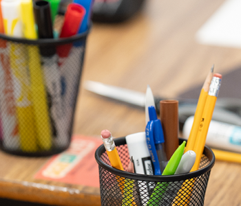 Student with papers and cups with pencils and markers