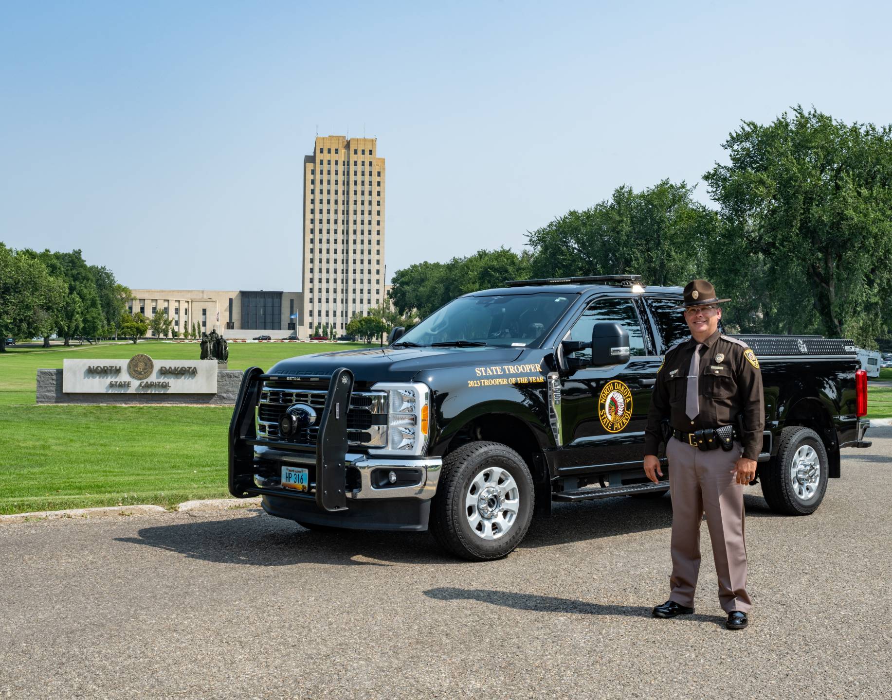 Trooper Myles Sundby standing in front of the state capitol building by his squad car.
