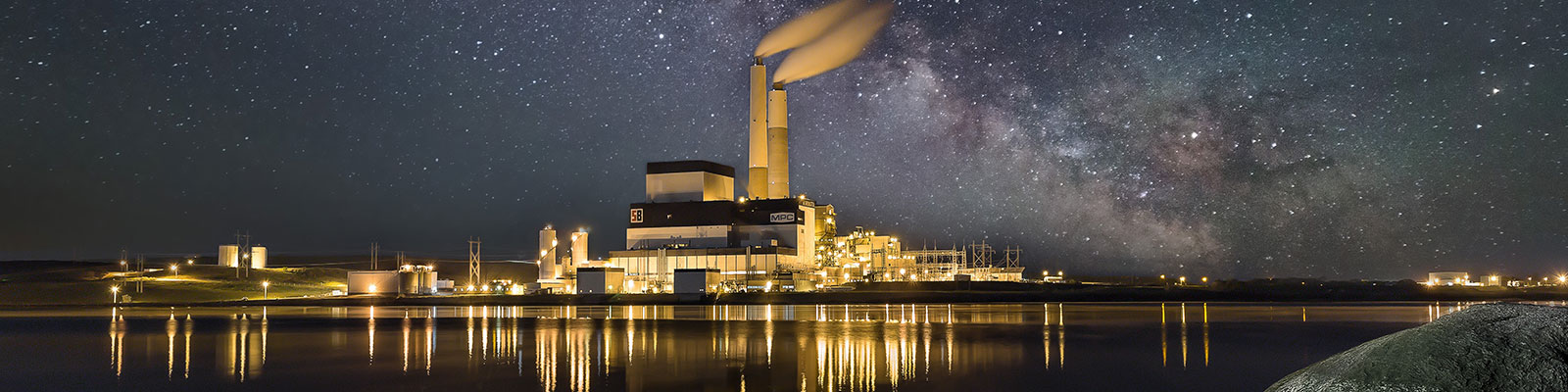 Power plant glows in the night against the starry night sky.