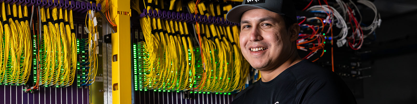 Man stands in front of data cables at a rural telecommunications company. 