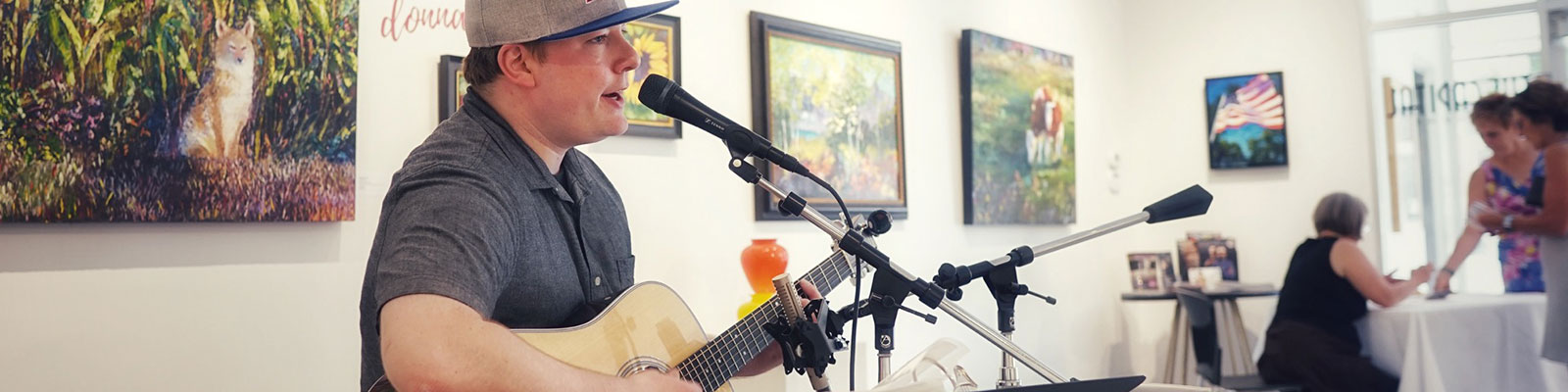 A musician sings and plays guitar at an art exhibit opening. 